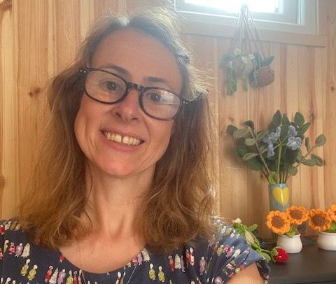 Val McFadden - Counsellor A woman with long brown hair smiles outdoors, wearing sunglasses, amidst greenery.
