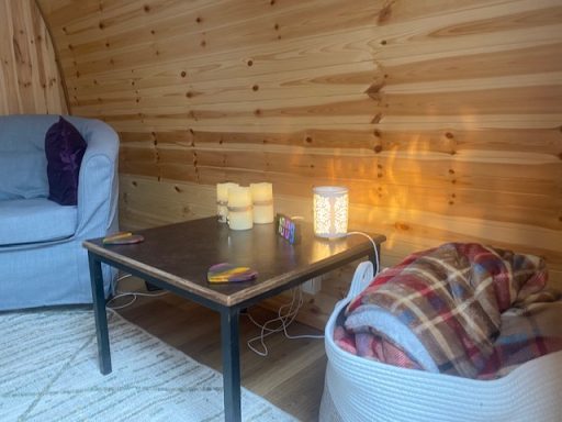 Inside The Therapeutic Camper Cozy interior with a sofa, table, candle, and a blanket in a wooden setting.