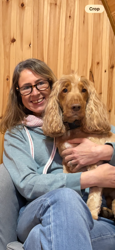 Val McFadden and Sonnie the Dog A woman with glasses smiles while holding a brown dog in a cozy setting.